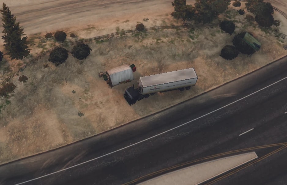 Aerial drone shot of a dark semi truck with a white trailer parked on scrubland beside an empty highway, next to an abandoned caravan